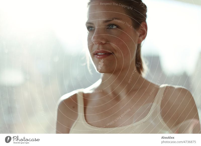 Backlight portrait of young tall blonde woman in front of window pane Tank top kind fortunate Central perspective Close-up Youthfulness look long hairs