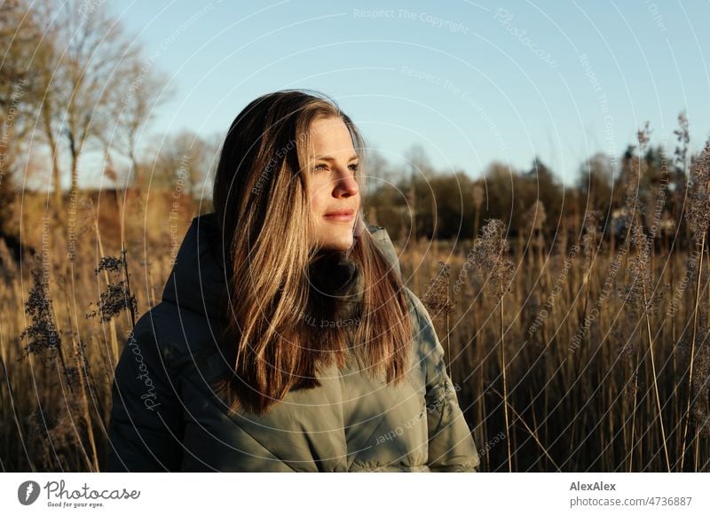 Tall blonde woman with long hair in warm light green jacket smiling very close to camera outside Landscape trees Grass Looking into the camera 18 - 30 years