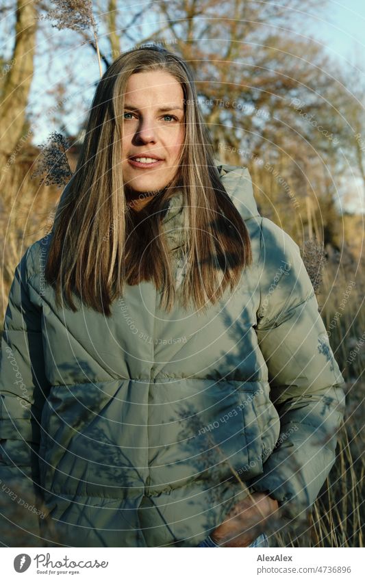 Tall blonde woman with long hair in warm light green jacket smiling very close to camera outside Landscape trees Grass Looking into the camera 18 - 30 years