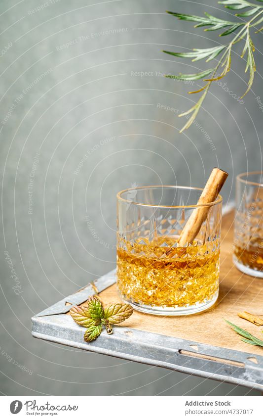 Glass of whiskey with cinnamon stick under plant branch glass spicy strong alcohol booze crystal serve glassware spice brandy corner flavor taste bourbon scotch