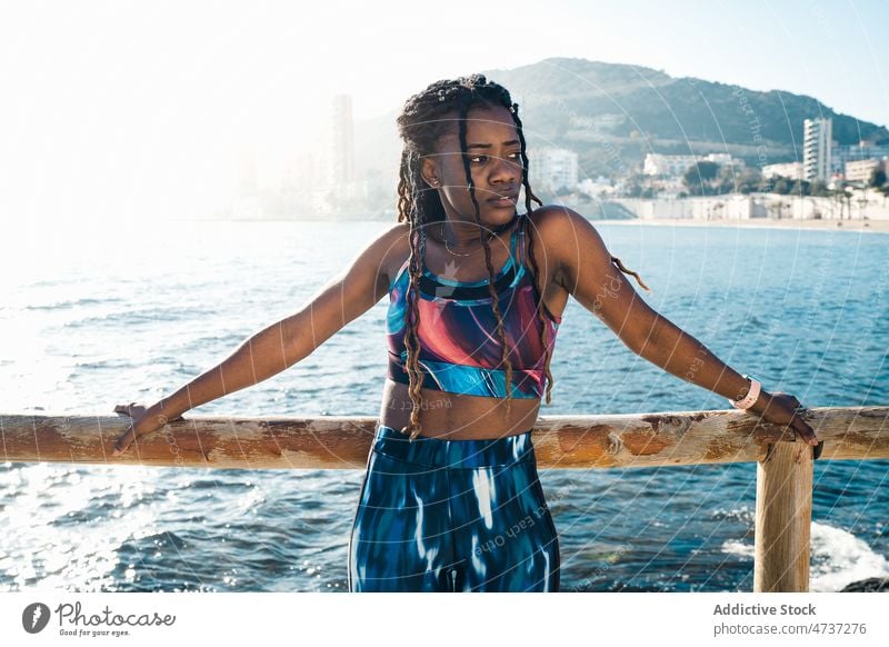 Serious black woman in sportswear leaning on fence on embankment fit sea training thoughtful wellness healthy activewear female sporty serious confident slim