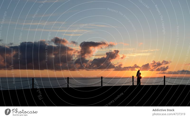 Couple standing on embankment and admiring sunset sky couple silhouette romantic sundown sea harmony admire love waterfront peace together romance shore coast