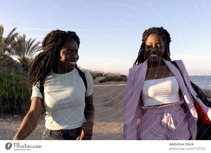 Cheerful black women walking on beach in sunset summer together friend lifestyle seashore evening female ethnic african american happy smile coast girlfriend