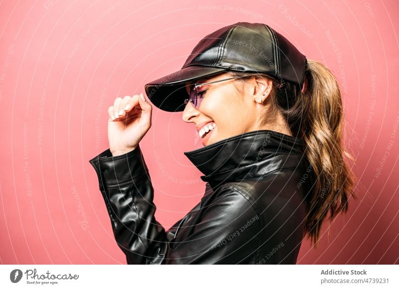 Glad lady against pink background woman leather jacket cap trendy style laugh delight studio model portrait cheerful smile female positive happy hispanic