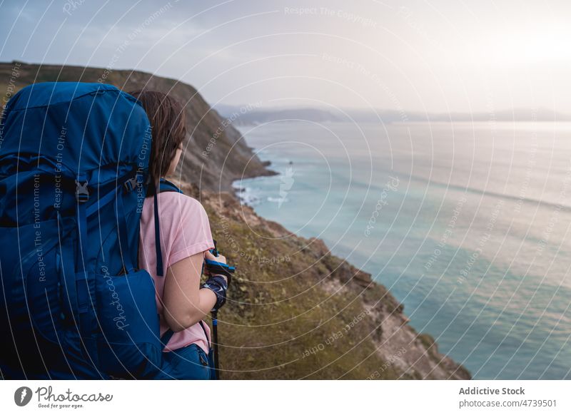 Anonymous hiker on shore at sunset time woman trekking adventure nature sea seashore waterfront pole sundown evening stick waterside seaside seafront backpack