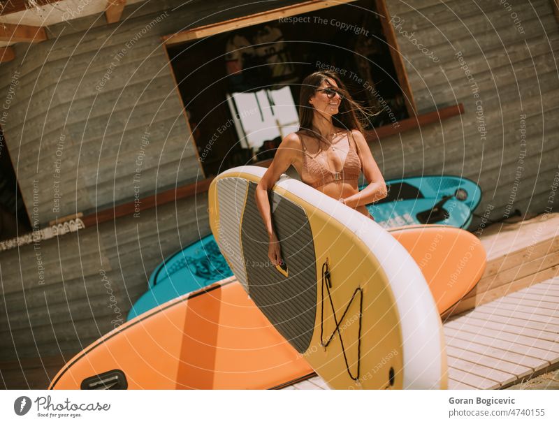 Young woman with paddle board on the beach on a summer day attractive beautiful bikini coast female fit friends friendship fun happy lifestyle ocean one outdoor