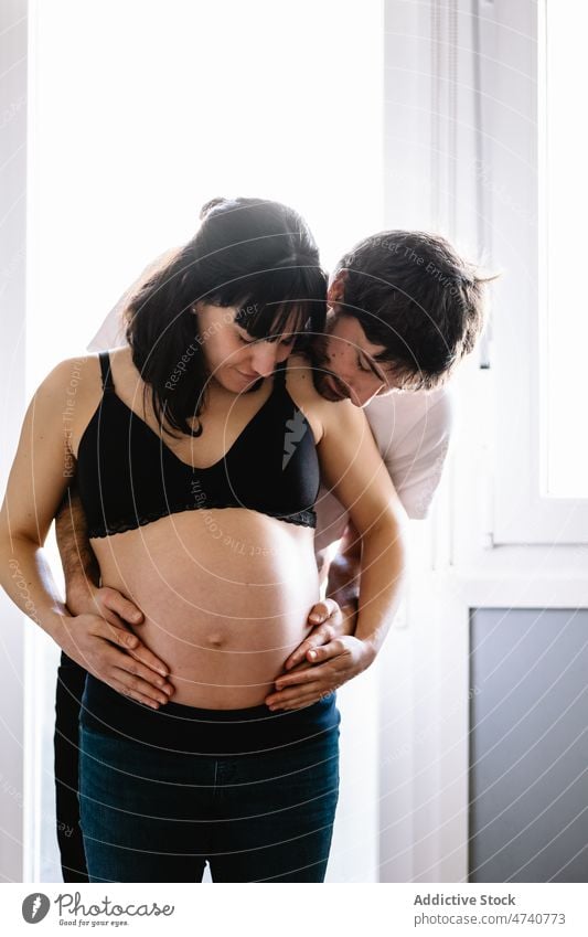 Cheerful man hugging pregnant woman at home couple embrace cheerful love pregnancy await anticipate tummy tender wife husband relationship together gentle happy