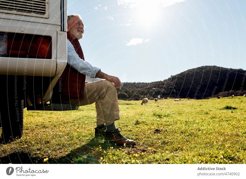 Mature man sitting near camper in nature motorhome car rv field road trip mature senior journey caravan trailer countryside transport parked male auto adventure