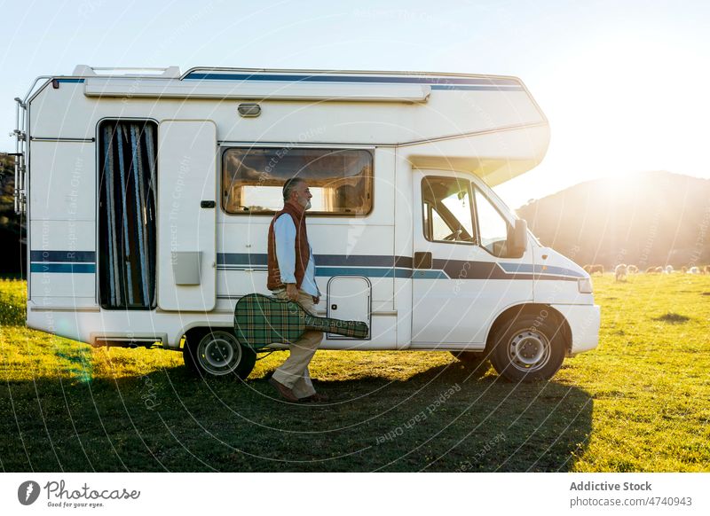 Man with guitar walking near camper man motorhome car rv nature road trip senior instrument hobby musical journey caravan trailer countryside transport parked