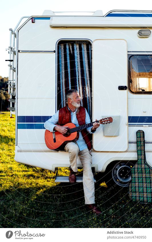 Senior man playing guitar in doorway of camper motorhome rv sit nature road trip senior instrument hobby song melody skill talent musical journey caravan