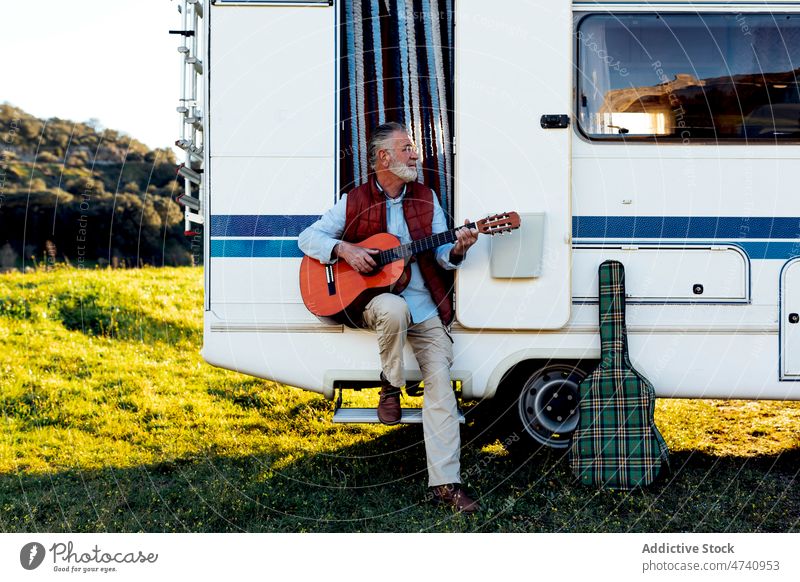 Senior man playing guitar in doorway of camper motorhome rv sit nature road trip senior instrument hobby song melody skill talent musical journey caravan