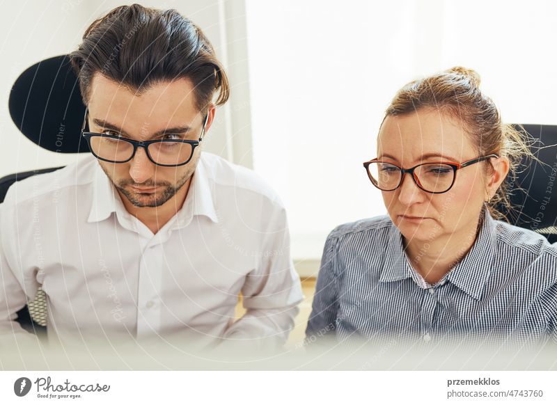 Two business people discussing financial data looking at computer screen. Entrepreneurs working hard sitting at computere screen in office. People having deadline working together