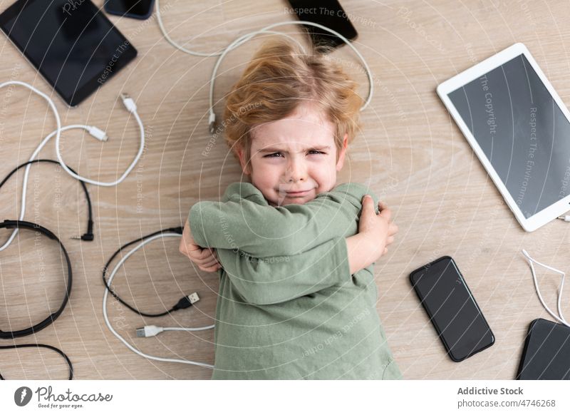 Crying boy amidst various gadgets cry upset cable dependency addiction punishment unhappy prohibit modern problem device kid smartphone tablet cellphone wire