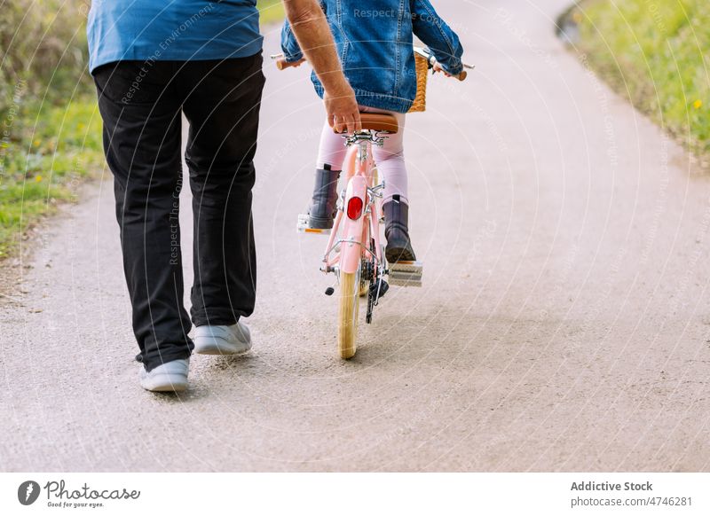 Anonymous grandfather teaching girl riding bicycle in countryside hobby leisure childhood spend time ride help spare time man care learn activity kid entertain