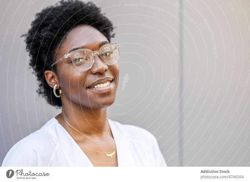 Content black woman in glasses and work uniform street city appearance style feminine urban eyewear wall african american female summer glad white enjoy