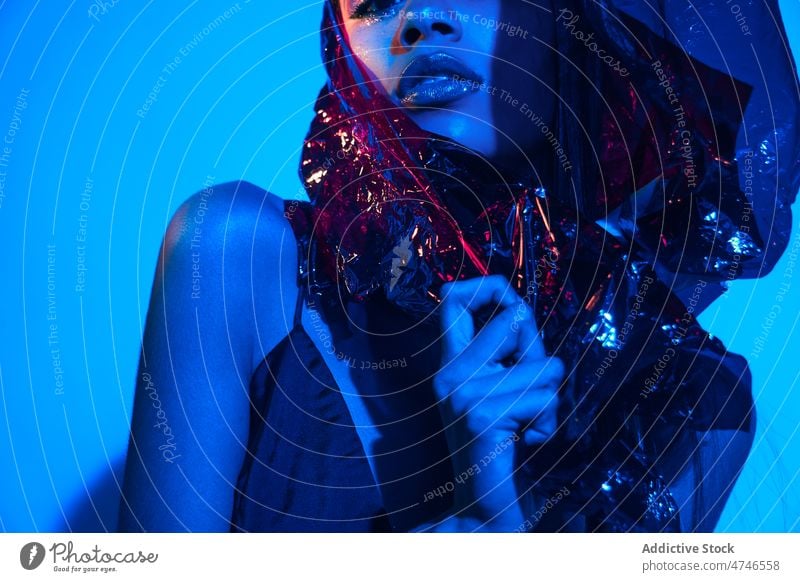 Fashionable woman wrapped in plastic in neon illumination model fashion provocative cool posture makeup female style blue light illuminate glow creative