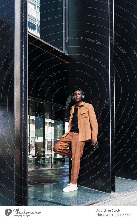 Stylish black man listening to music near building headphones street style song melody pastime hobby african american male city wireless trendy urban audio