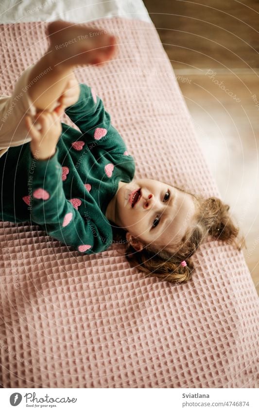 A cute little girl is lying on the bed with her leg raised and straightens her panties fun female child morning portrait hair indoor face emotional day cheerful