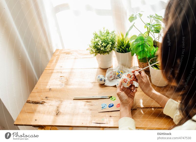 Female painting a modern easter eggs. Brushes and paints with flowers and plants. Happy easter concept on a wooden background. hands painted celebration female