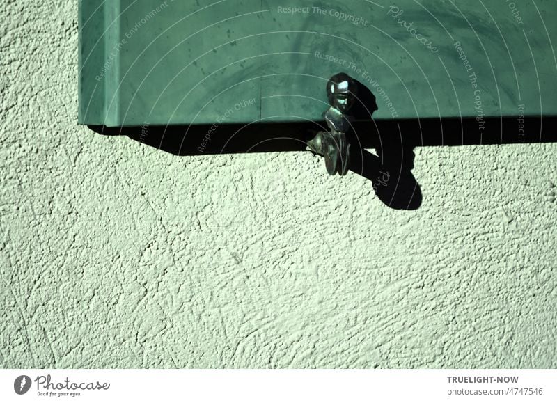 Shiny iron window shutter holder in afternoon sun with strong shadow on lime green house wall and blue green or mint colored wooden window shutter