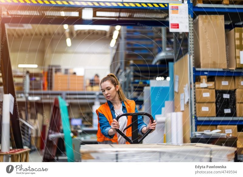 Young worker moving goods on pallet jack at warehouse business cargo confident delivering delivery distribution employee factory female industrial industry job