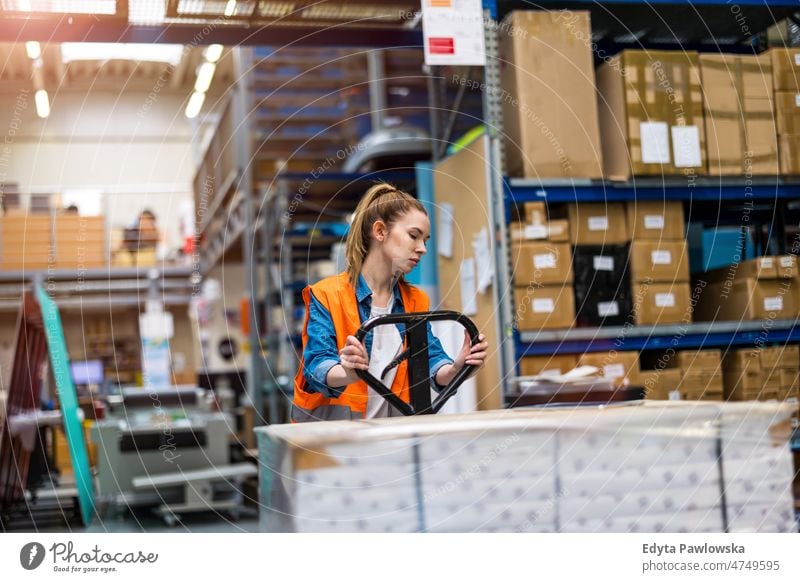 Young worker moving goods on pallet jack at warehouse business cargo confident delivering delivery distribution employee factory female industrial industry job