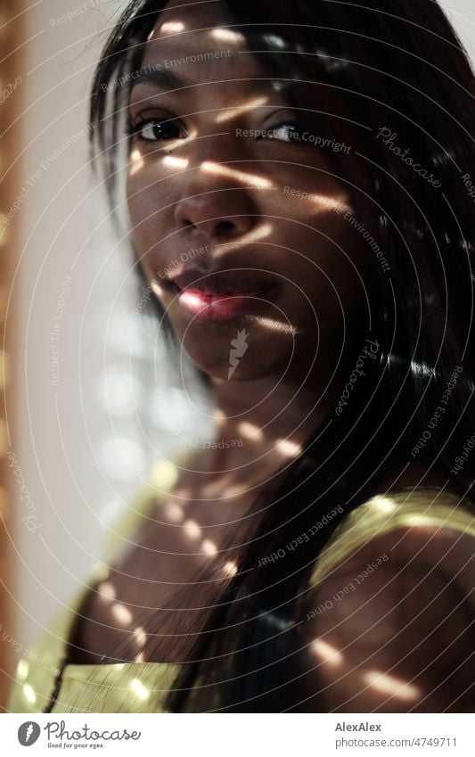 Young beautiful long haired woman in yellow summer dress stands in front of half closed blinds, light streaks on her face Woman Young woman pretty