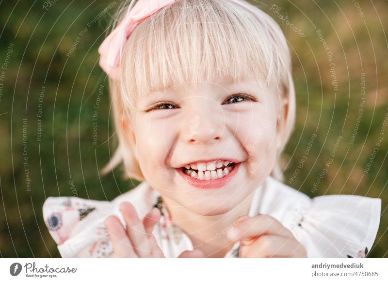 Portrait of a little laughing beautiful girl on nature on summer day vacation. child in dress is playing in the green park at the sunny time. The concept of family holiday and time together