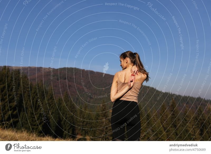 Young athletic woman stretching before intense morning workout at sunset or sunrise in beautiful mountain location. The concept of energy, health and harmony during sports