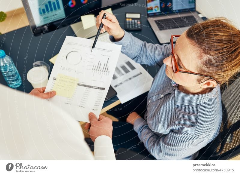 Businesswoman discussing financial data with her colleague sitting at desk in office. Woman entrepreneur working with charts and tables on computer. Two people working together