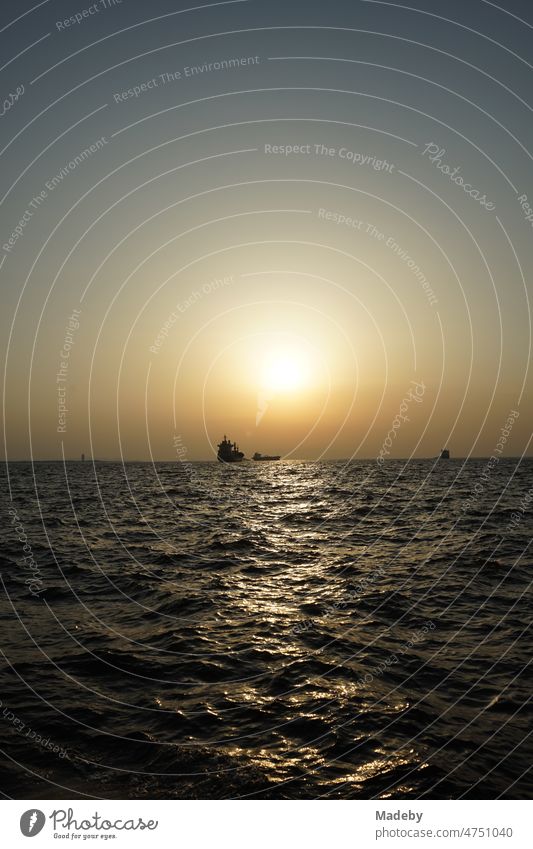 Anchoring cargo ship in the bay of Izmir in the light of the setting sun over the Aegean Sea in summer in Turkey Returning home Kitsch Evening world trade