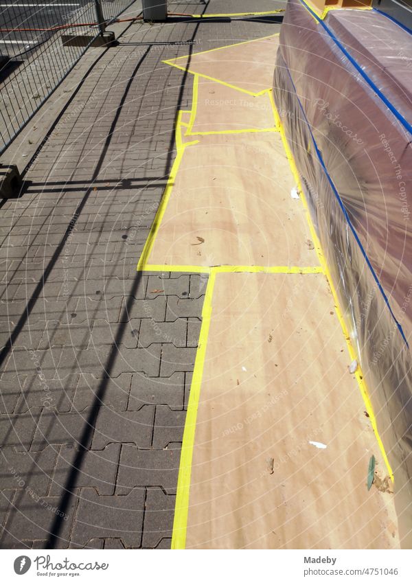 Taped facade and paving stones of the sidewalk with foil during painting work on an old building in summer sunshine in the north end of Frankfurt am Main in Hesse, Germany