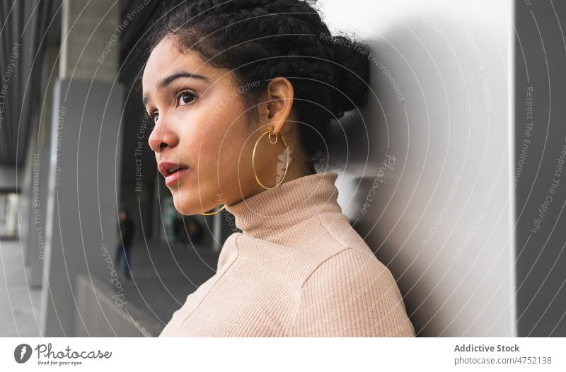 Charming ethnic woman leaning on wall and looking away curious style charm individuality stare millennial gaze modern interest female urban serious appearance