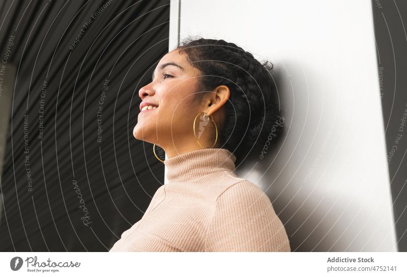 Charming ethnic woman leaning on wall and looking away curious style charm individuality stare millennial gaze modern interest female urban appearance happy