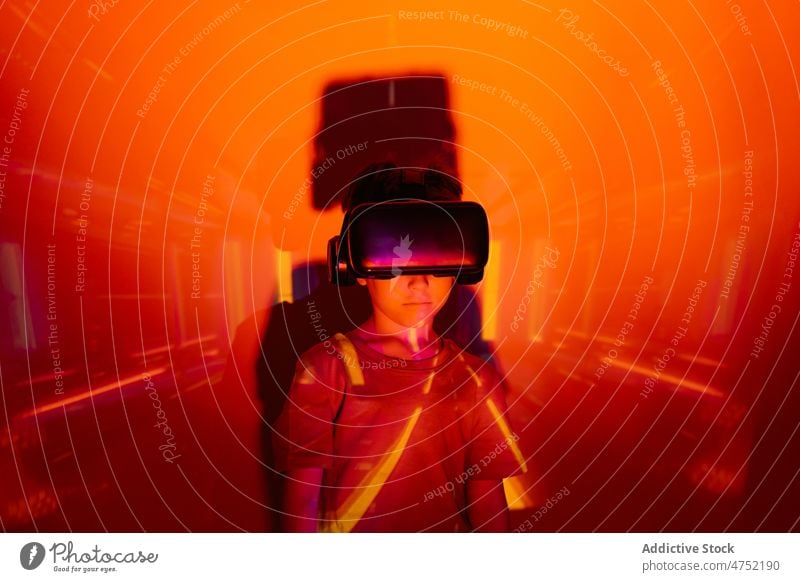 Little gamer in VR glasses boy vr lean wall watch videogame explore red light neon illuminate color child kid monochrome bright headset entertain