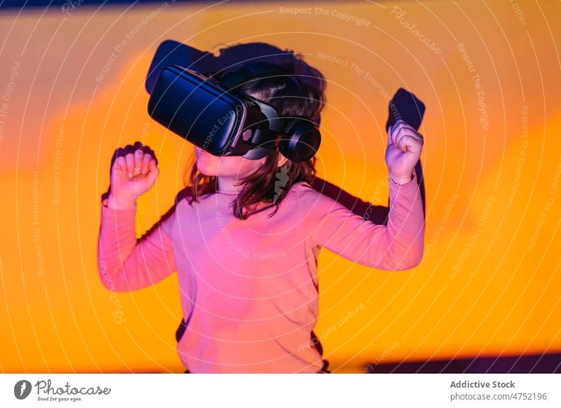 Little gamer celebrating victory in VR game girl celebrate success vr clench fist experience neon illuminate kid videogame child winner digital gadget entertain