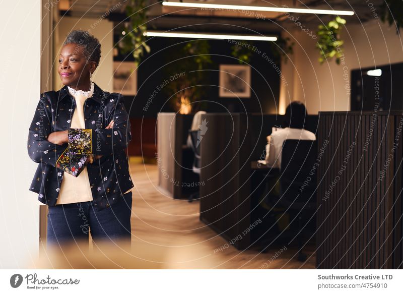 Portrait of confident senior black woman with arms folded smiling and looking out of window in coworking space Woman owned business portrait empowerment