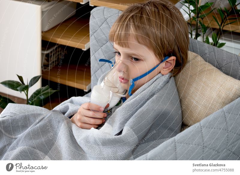 Little caucasian boy making inhalation with nebulizer at home. Child holds a mask vapor inhaler. Treatment of asthma. Concept of inhalation therapy apparatus.