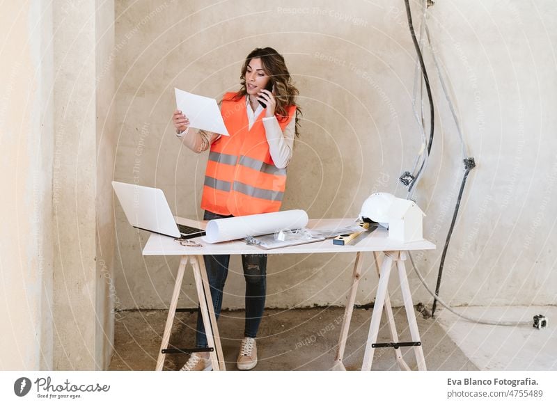 professional architect woman in construction site talking on mobile phone holding blueprints workspace protective helmet protective jacket real estate caucasian