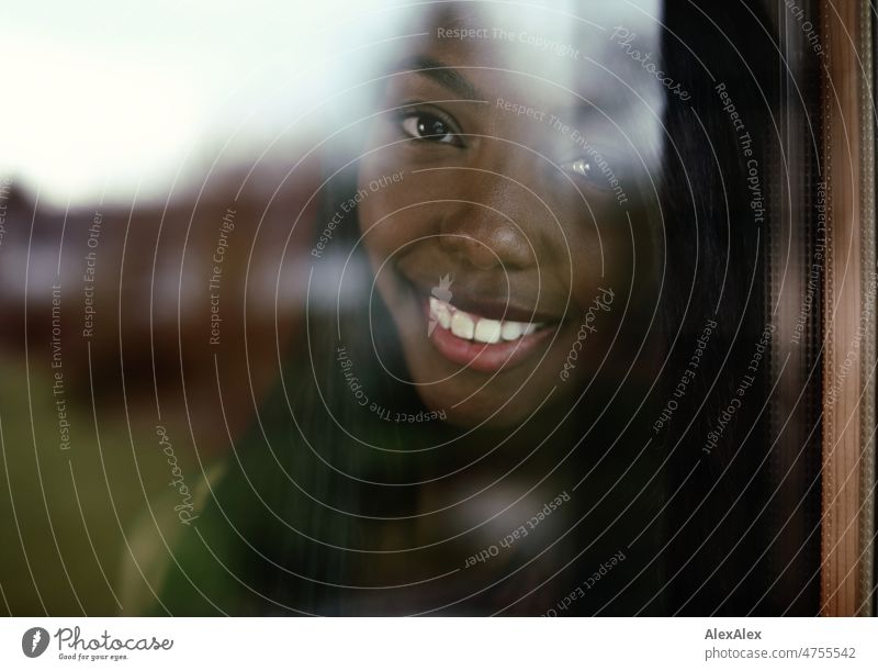 Young beautiful long haired woman stands behind the window and smiles out Woman Young woman pretty Beauty & Beauty Graceful Joy Friendliness kind fortunate PoC