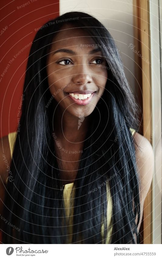 Young beautiful long haired woman in yellow summer dress stands in front of red wall at window and smiles at camera Woman Young woman pretty Beauty & Beauty