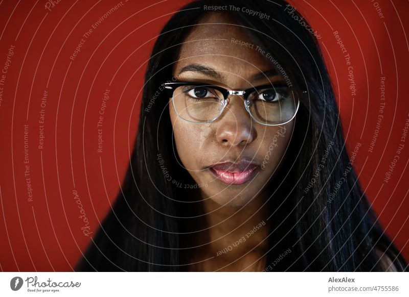 Young beautiful long haired woman with retro glasses stands in front of red wall and looks seriously and directly into camera Woman Young woman pretty