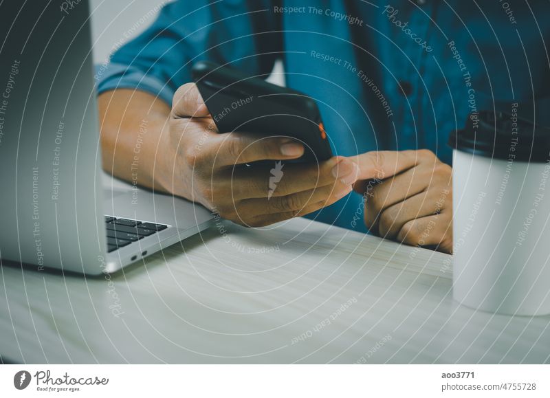 A man holding a smartphone and a laptop to search the Internet, send text messages, use an SMS messenger or do online banking. Businessman labour Communication