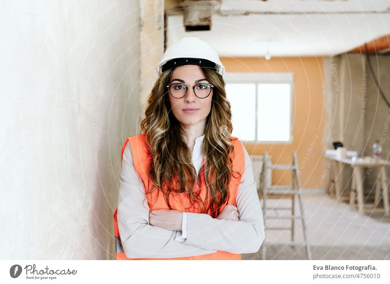 professional confident architect woman in construction site with arms crossed. Home renovation blueprints workspace protective helmet protective jacket