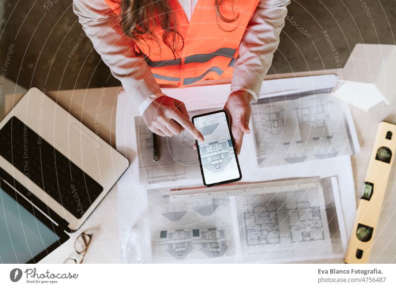 top view of professional architect woman in construction site working on mobile phone and blueprints unrecognizable workspace protective helmet