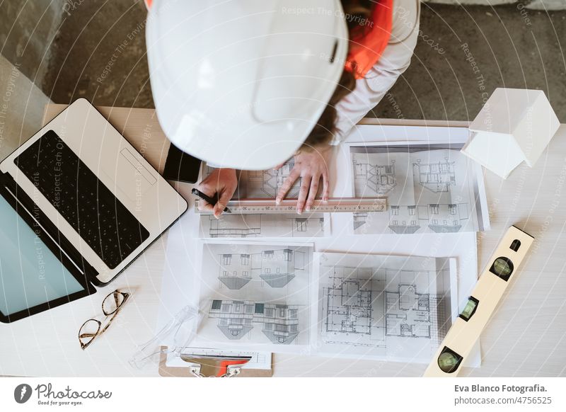 top view of professional architect woman in construction site working on laptop and blueprints unrecognizable mobile phone workspace protective helmet