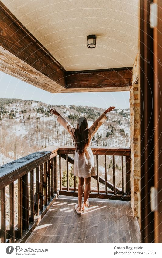 Charming young woman in bathrobe enjoying the winter nature on the large terrace rear view back cold balcony white outdoor background snow holiday beautiful