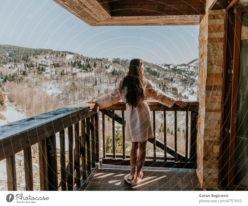 Charming young woman in bathrobe enjoying the winter nature on the large terrace rear view back cold balcony white outdoor background snow holiday beautiful