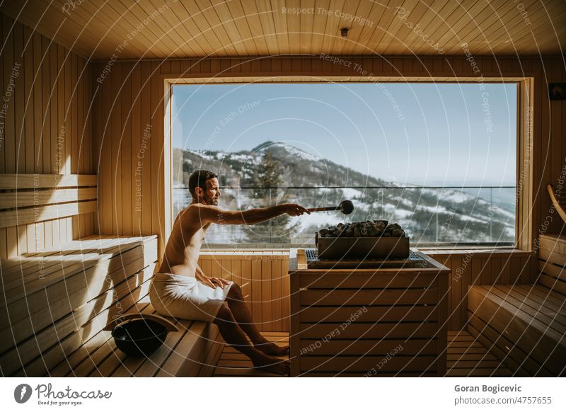 Young man pouring water onto hot stone in the sauna activity adult bath bathhouse beard bearded beauty bench body caucasian comfortable enjoyment handsome