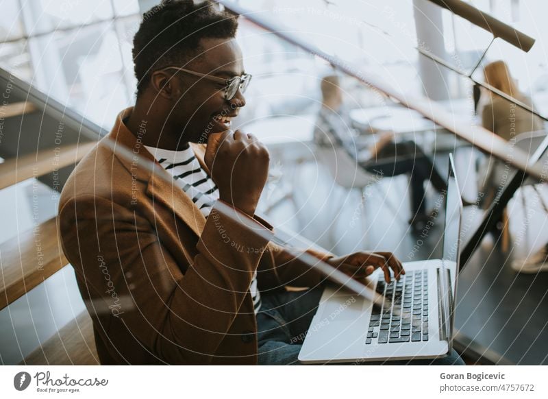 Young African American business man working on laptop computer while sitting on a office stairs african american black brainstorming obnline businessman